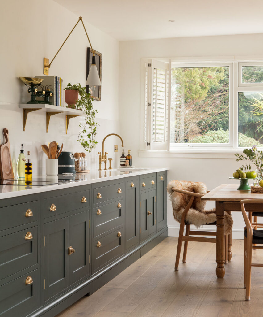 Dark green kitchen with brass accents, natural light and wall decor including open shelving and accent lighting