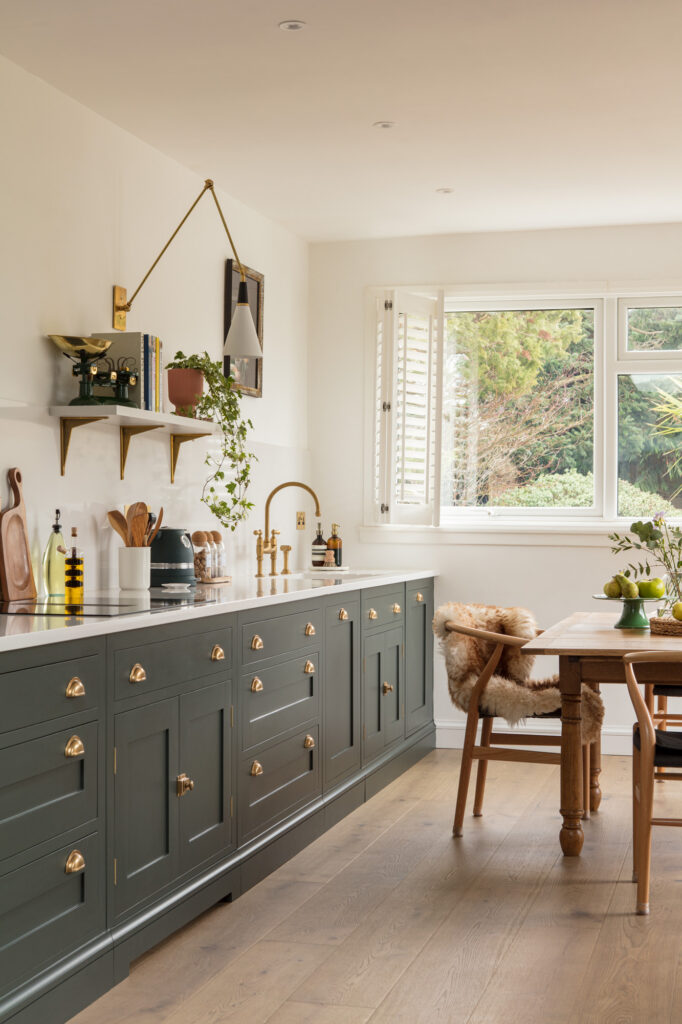 Dark green galley kitchen with brass hardware, quatz worktop and small dining table