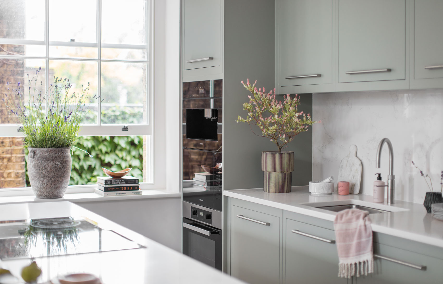 Light blue green contemporary kitchen design with white worktops and built in ovens