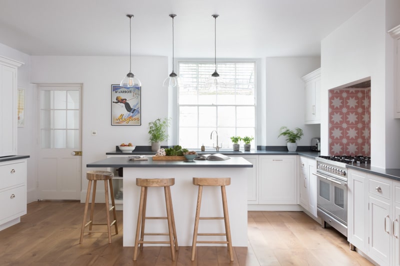 Harvey Jones White Srbor kitchen featuring black worktops and wooden smile stools around a kitchen island