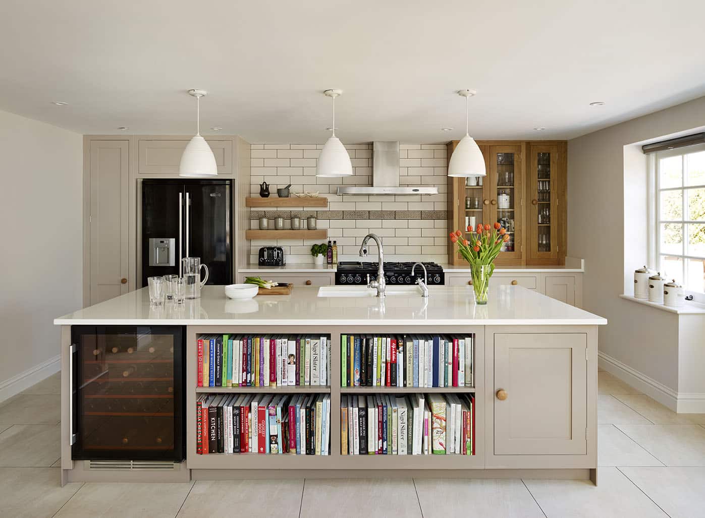 Warm neutral-toned Shaker kitchen design featuring beige kitchen island with book shelving and integrated wine fridge
