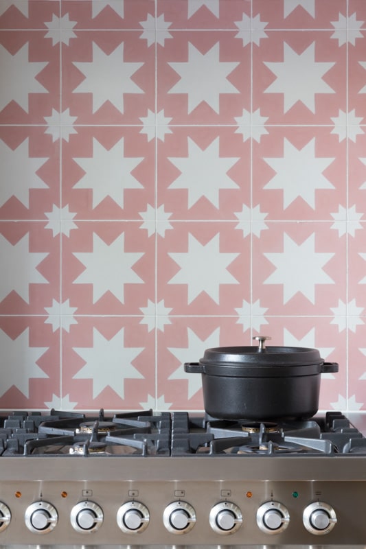 Decorative pink and white tiling behind a silver cooker top