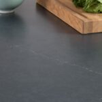 Black worktop featuring a wooden chopping board and fresh vegetables