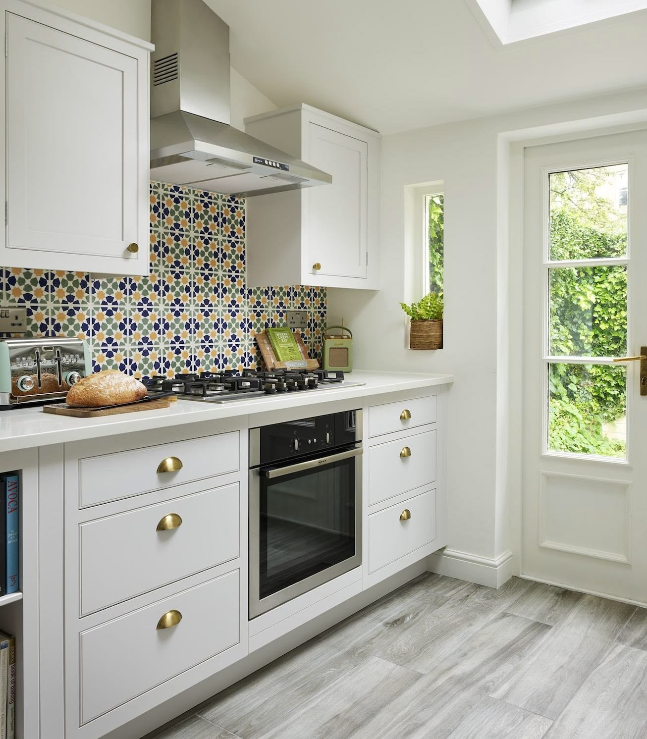 White galley style kitchen featuring white Arbor cabinetry with decorative tiling behind a cooker area