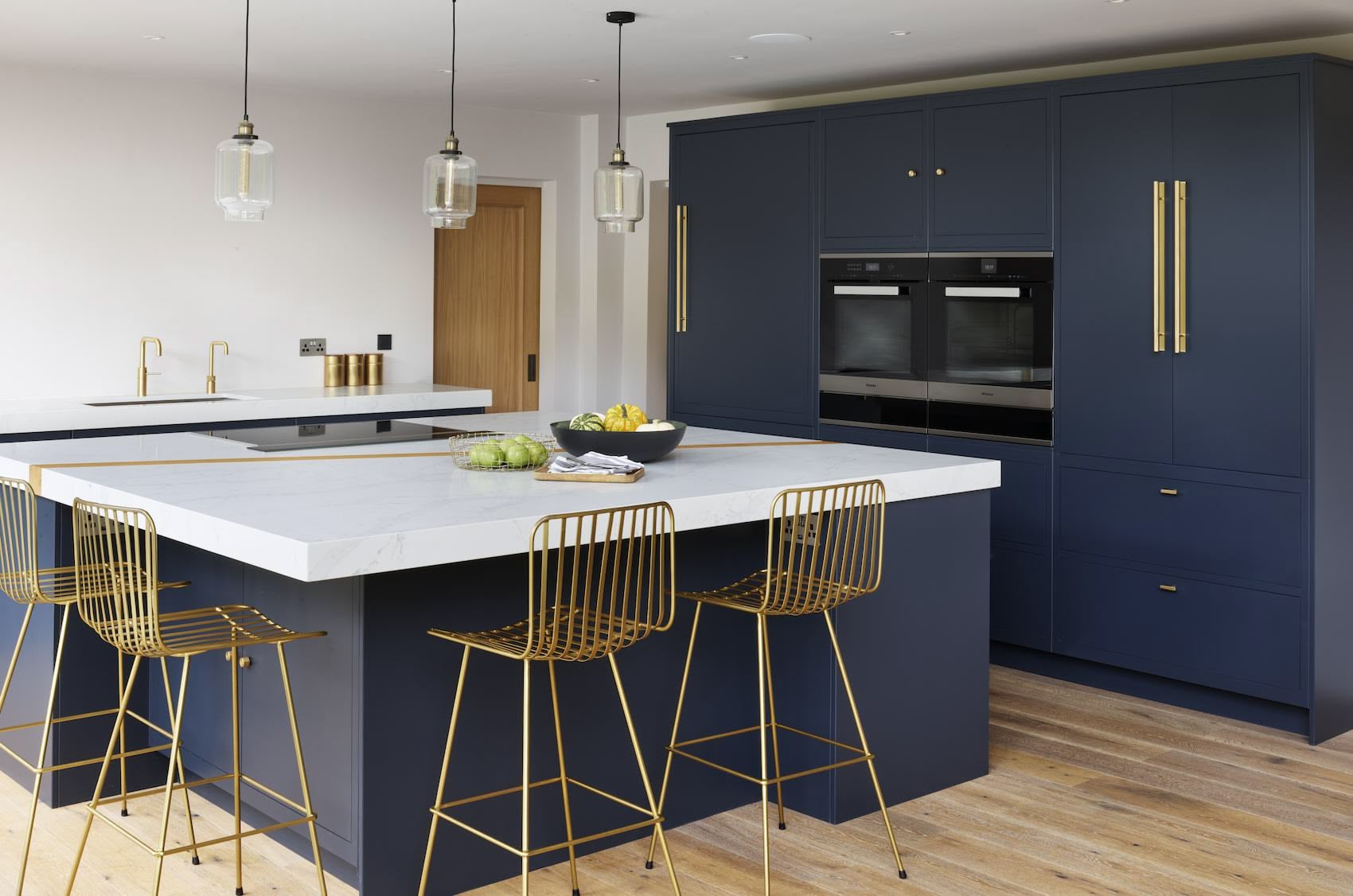 Blue kitchen island with white worktop and gold stools