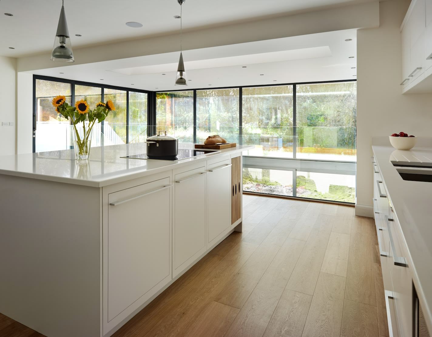 White Linear family kitchen with floor to ceiling windows overlooking the garden