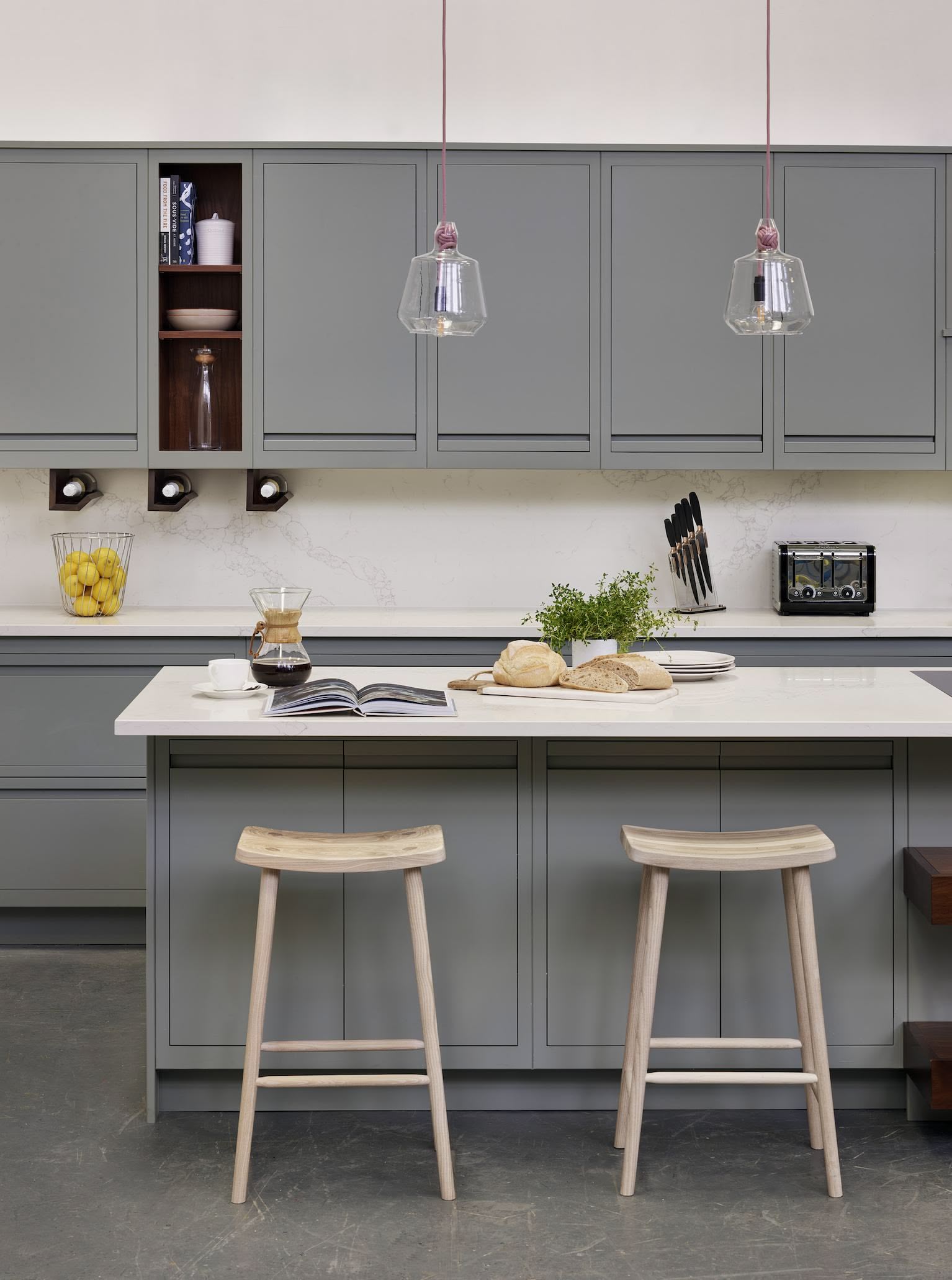 Green-grey kitchen island with white worktop featuring natural wooden smile stools
