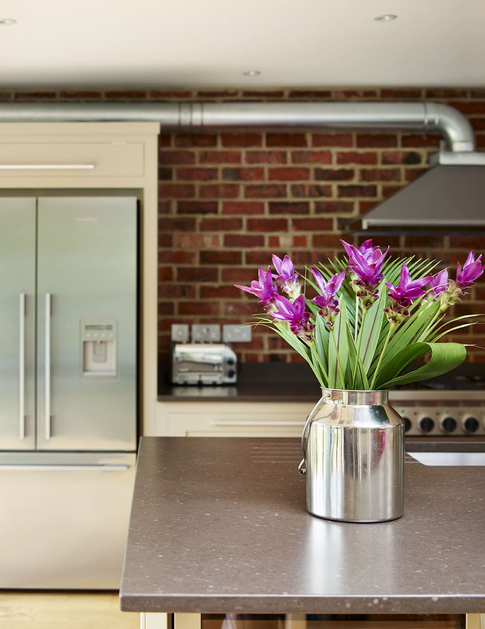 Grey kitchen island worktop featuring Shaker kitchen cabinetry and exposed brick wall