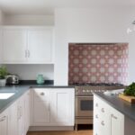 White Arbor kitchen cabinetry and black worktops with decorative tiling around the cooker area