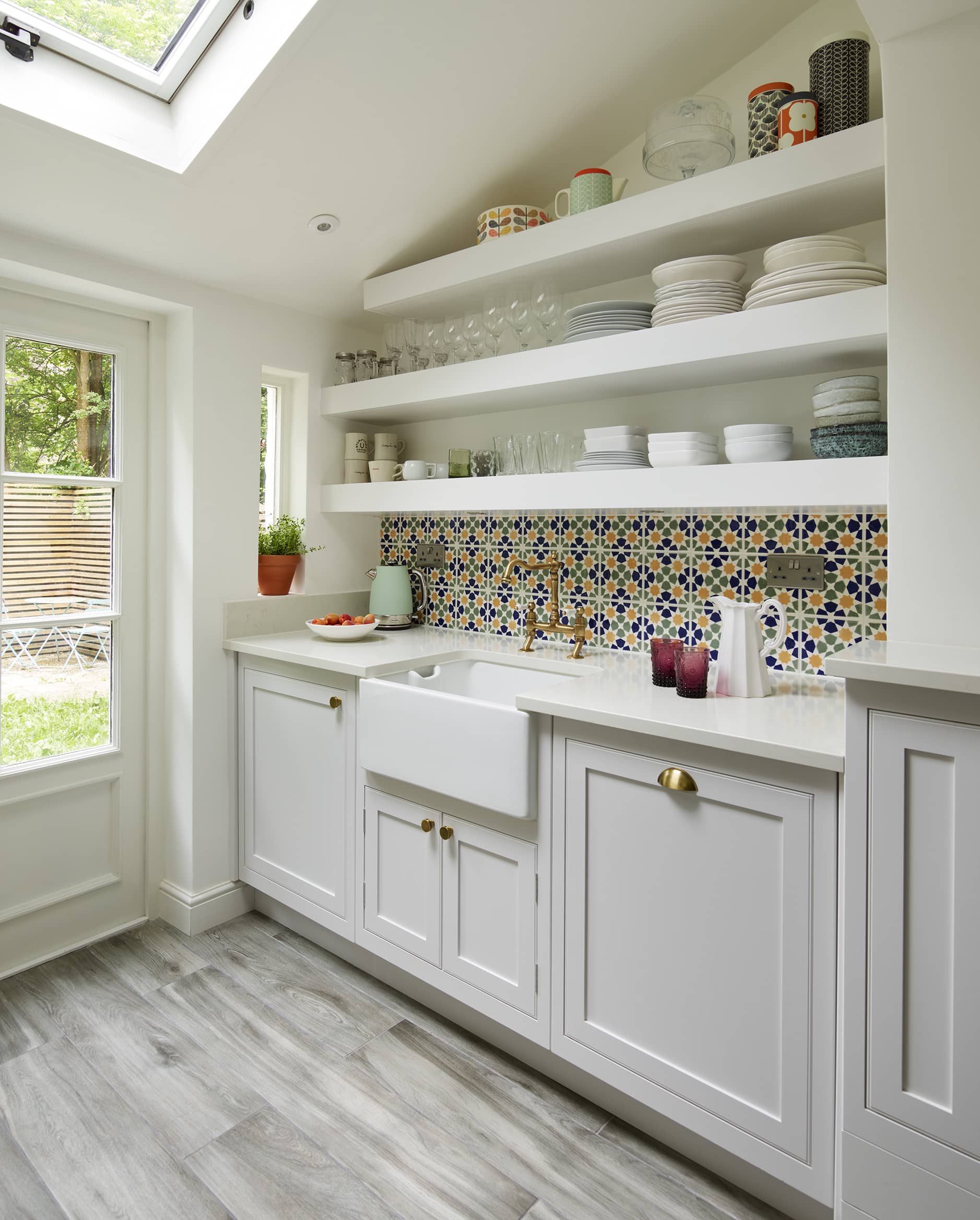 White galley style kitchen featuring white Arbor cabinetry around a white basin sink with a decorative tiled splashback