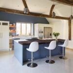 Blue kitchen island with white worktop and black extension featuring white stools