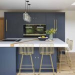 Blue kitchen island with a white worktop, integrated hob and gold stools