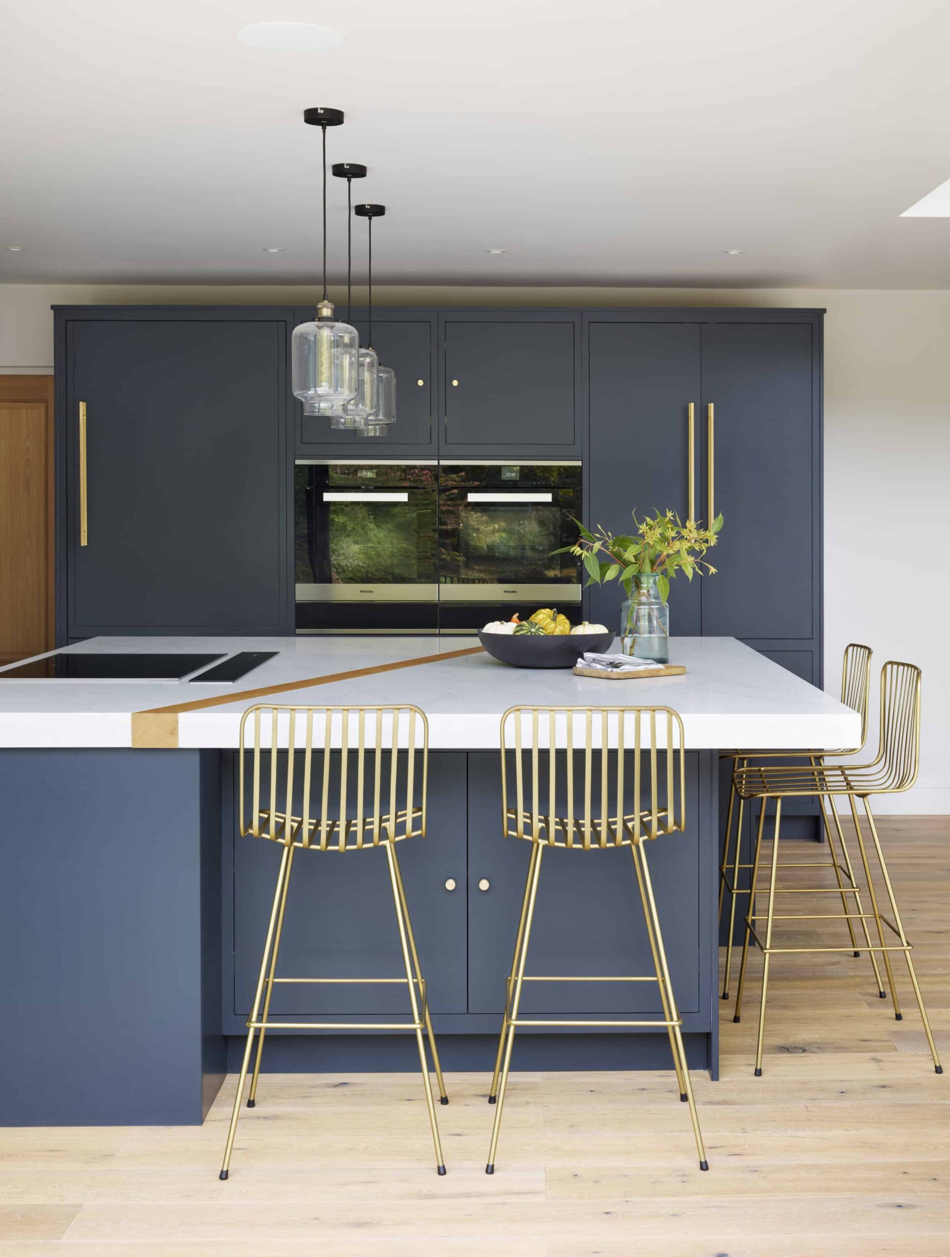 Blue kitchen island with a white worktop, integrated hob and gold stools