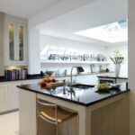 White Shaker kitchen island with black worktop featuring integrated sink and bar stool