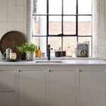 Cream Linear Edge kitchen cabinetry with white marble worktop featuring a white sink with dark tap against a window