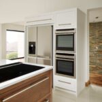 Walnut kitchen island with integrated hob and white kitchen cabinetry containing appliances