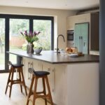 White Shaker kitchen island with grey worktop featuring integrated sink and black and oak bar stools