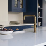 Navy Shaker kitchen cabinetry with white worktops featuring integrated sink and brass tap