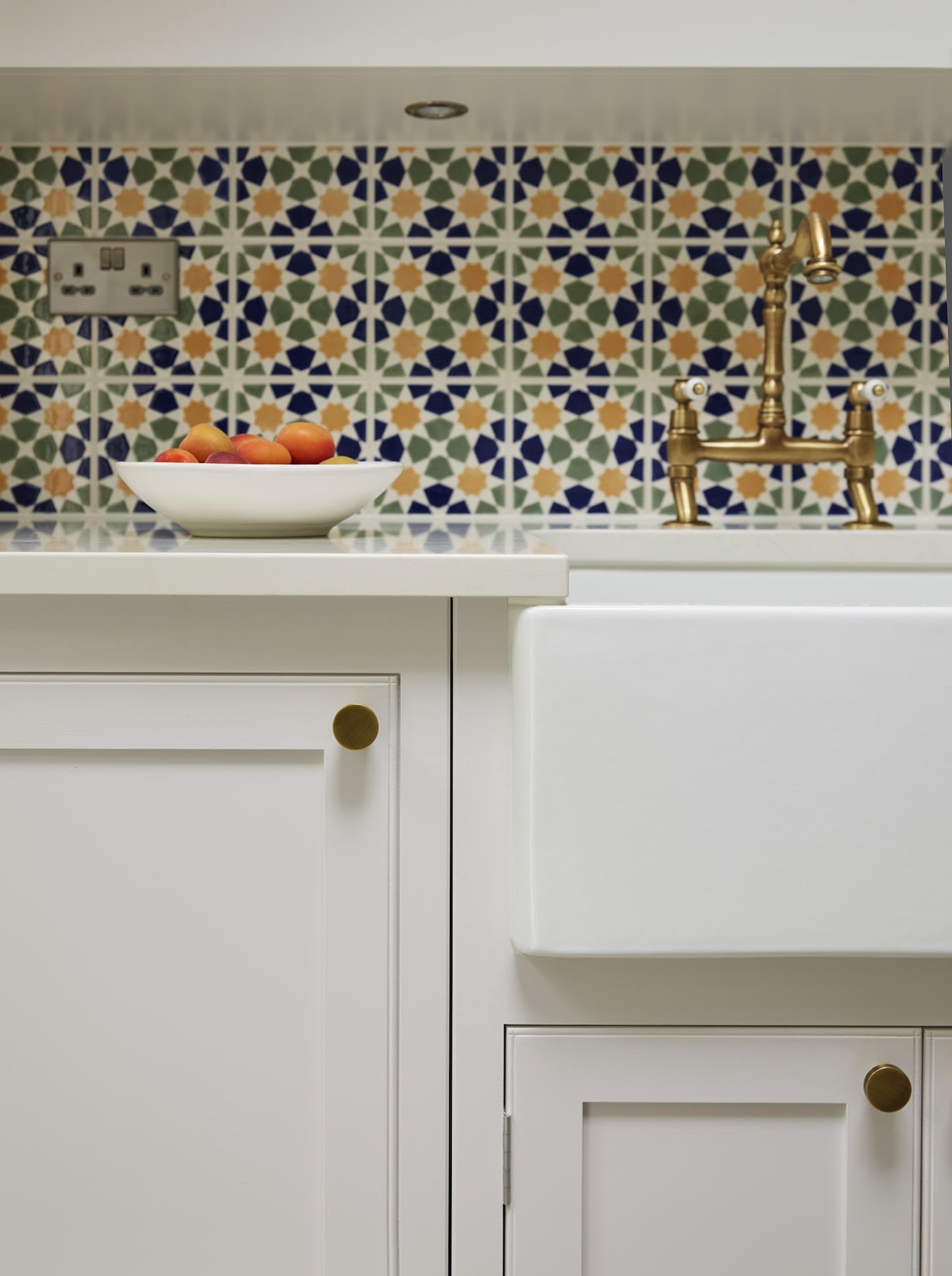 White Arbor kitchen cabinetry around a white basin sink featuring a gold tap and decorative colourful tiles