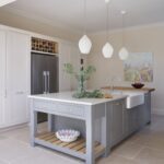 Grey kitchen island featuring a grey marble worktop and white cabinetry featuring an American style fridge with wine storage above