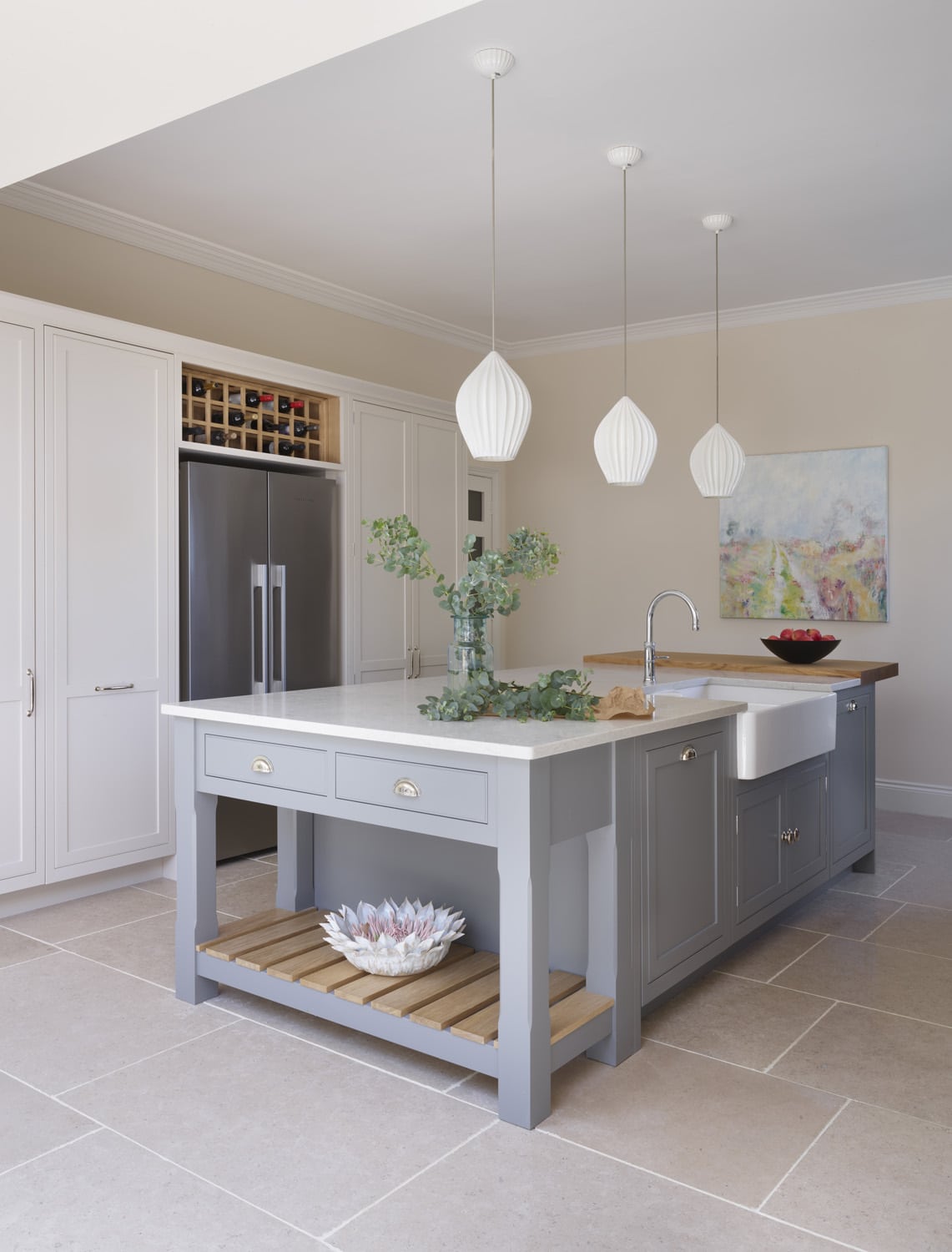 Grey kitchen island featuring a grey marble worktop and white cabinetry featuring an American style fridge with wine storage above