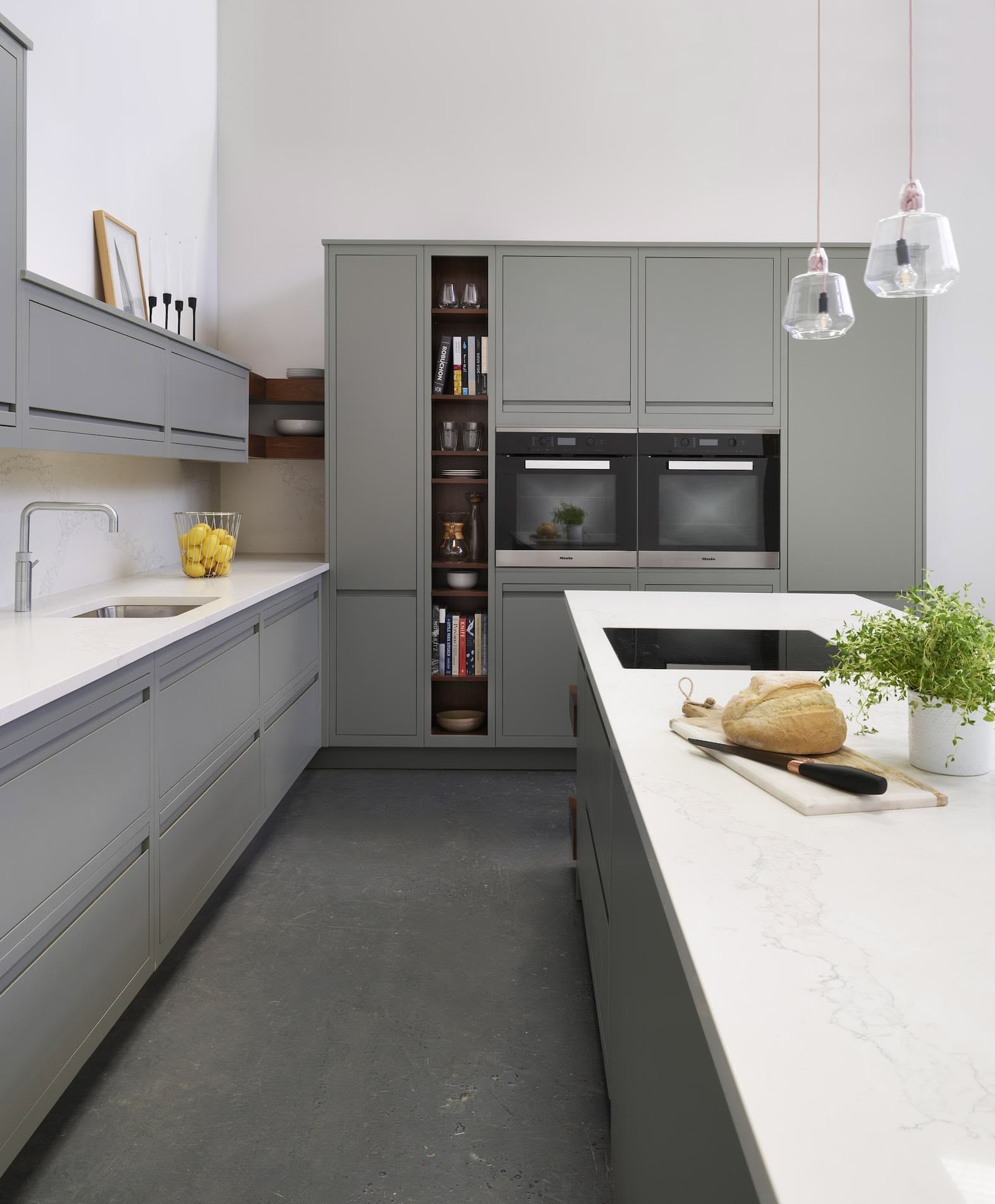 Green-grey kitchen cabinetry containing double oven and dark oak shelving