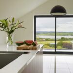Walnut kitchen island with white worktop and integrated hob overlooking large windows
