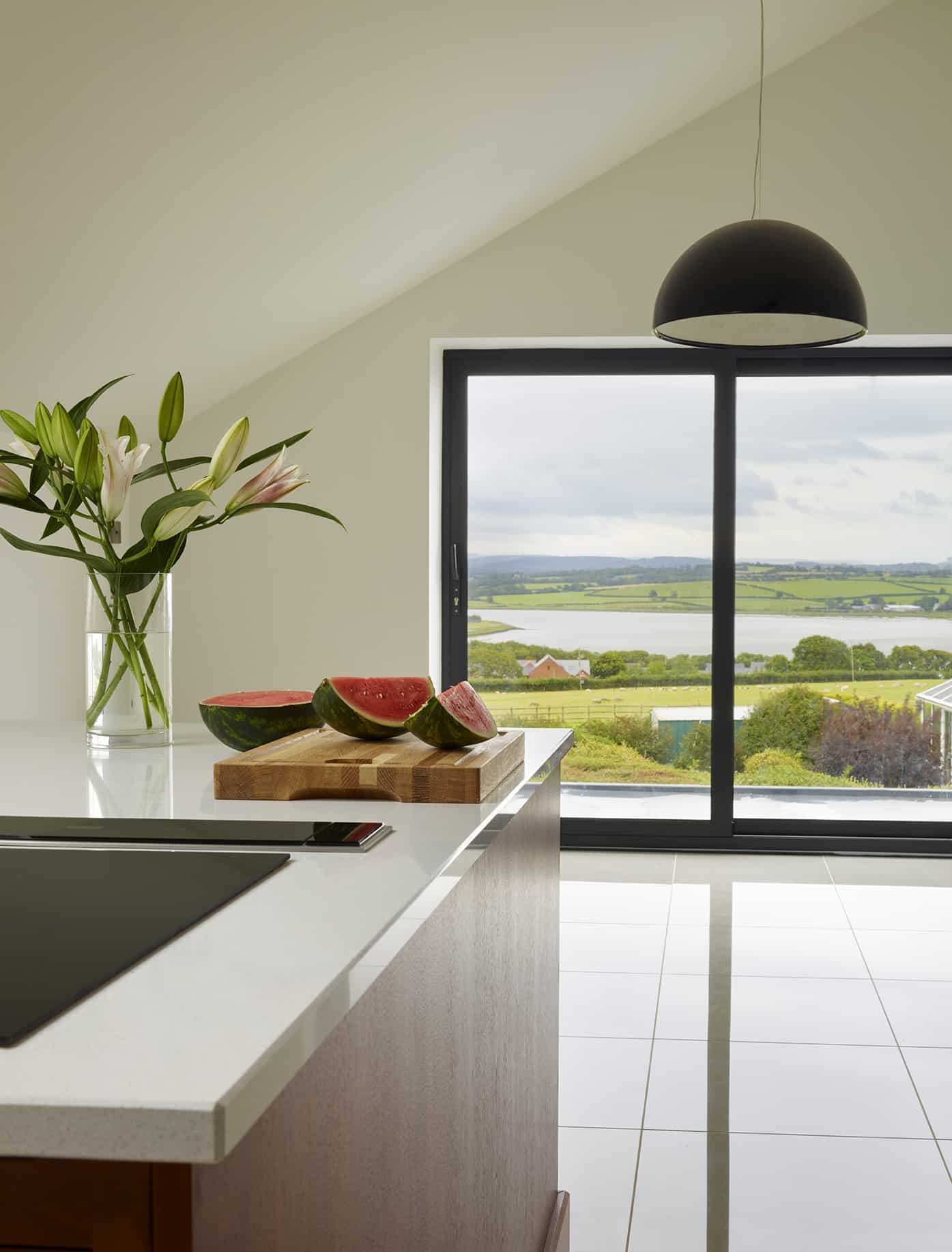 Walnut kitchen island with white worktop and integrated hob overlooking large windows