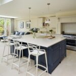 Blue kitchen island with white worktop and white stools next to open plan living area