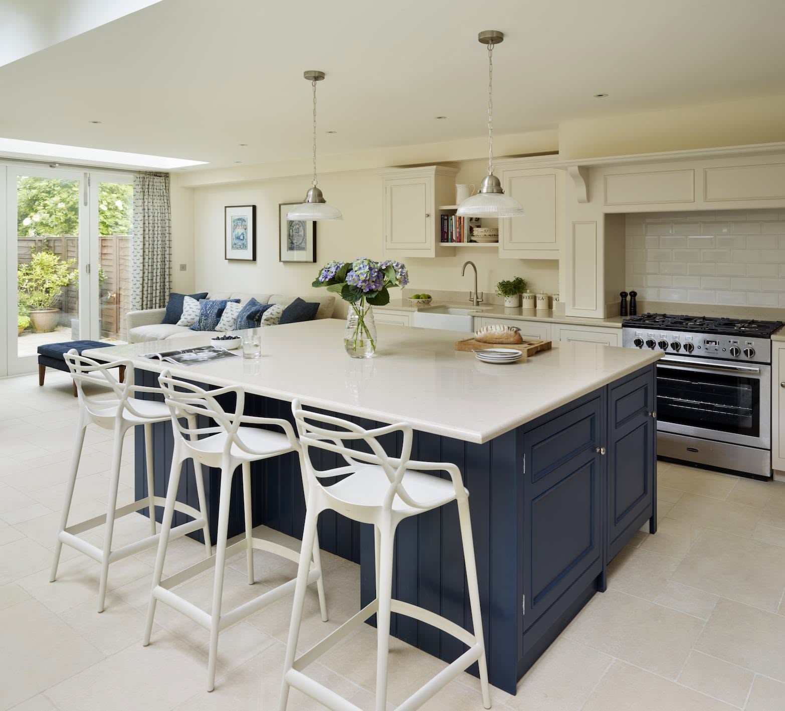 Blue kitchen island with white worktop and white stools next to open plan living area