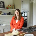 Female stood against Shaker kitchen island with walnut worktop