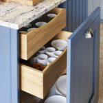 Closeup of blue Shaker kitchen cabinetry open to reveal light oak interior and organised storage