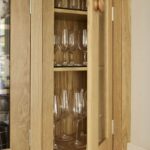 Oak overhead Shaker kitchen cupboard with glass doors open to show organised glassware