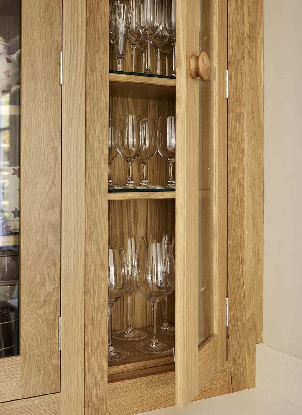 Oak overhead Shaker kitchen cupboard with glass doors open to show organised glassware