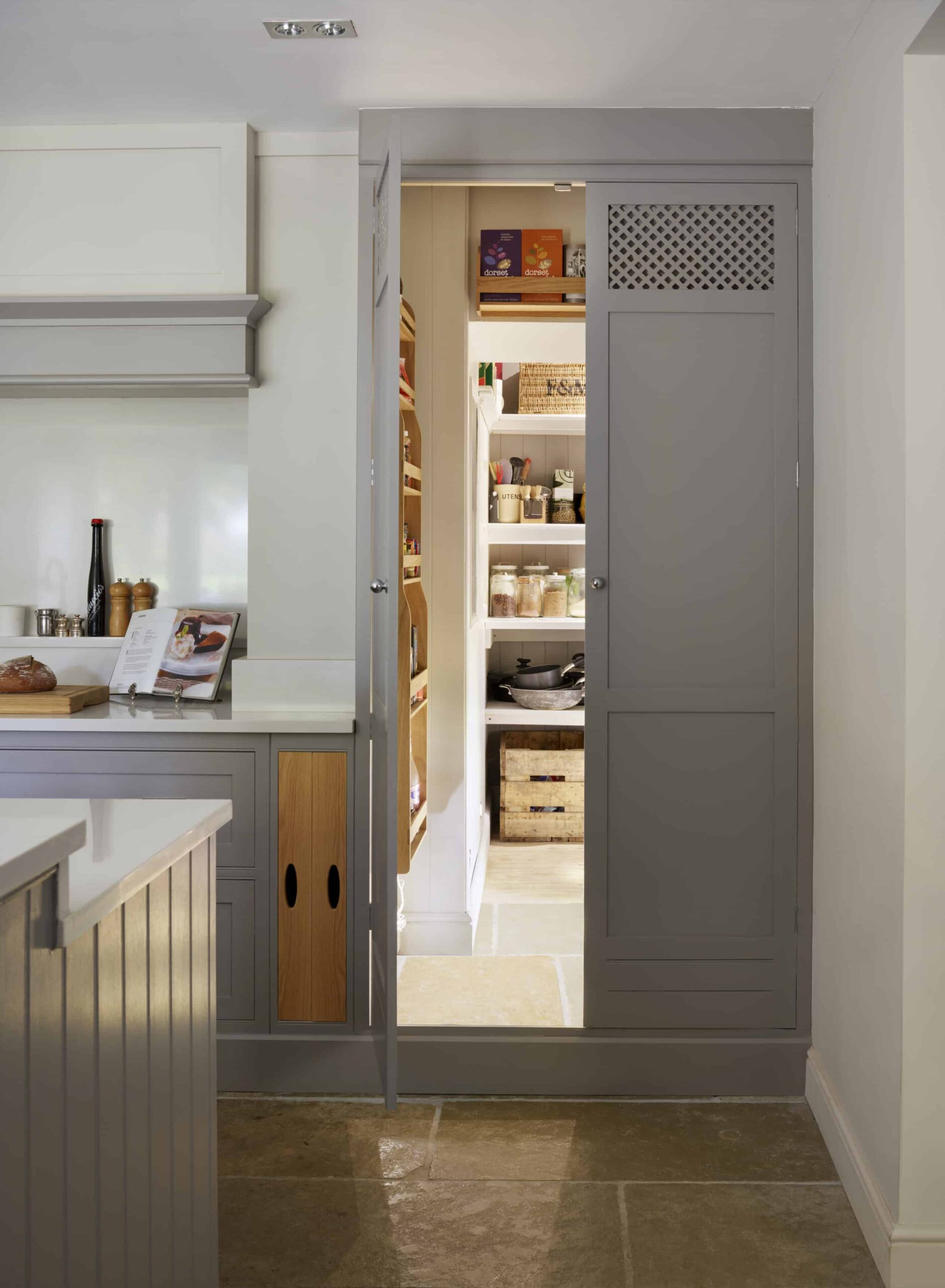 Tall grey pantry on the end of a kitchen worktop, open to show organised storage and drawers