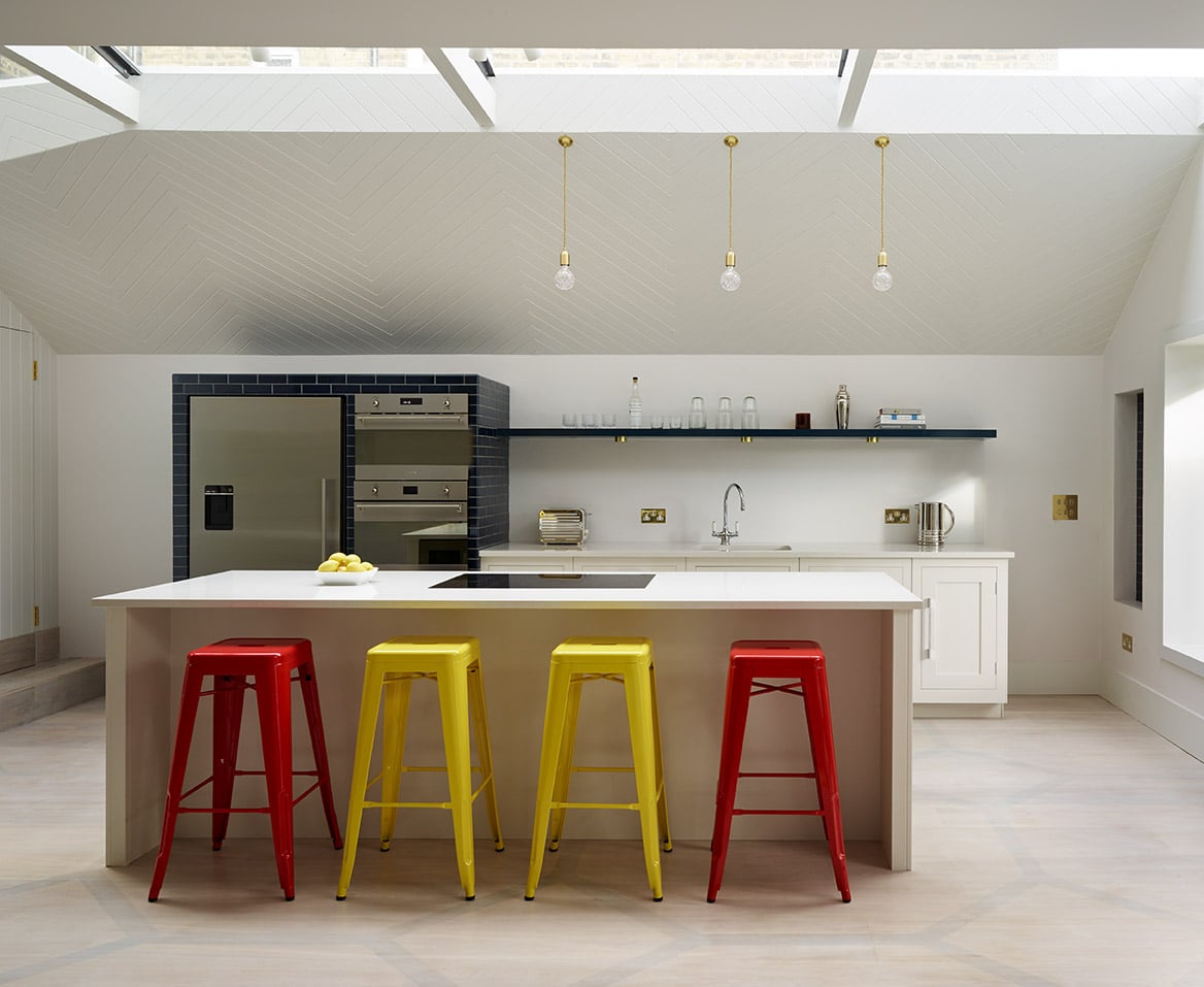 White Shaker kitchen island with white worktop featuring integrated hob and red and yellow bar stools