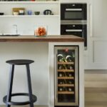 White Shaker kitchen island with walnut worktop featuring black bar stool and wine fridge