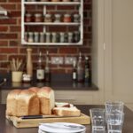 Shaker kitchen island with stacked crockery overlooking an exposed brick wall with organised shelving