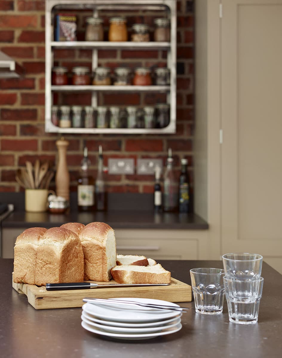 Shaker kitchen island with stacked crockery overlooking an exposed brick wall with organised shelving