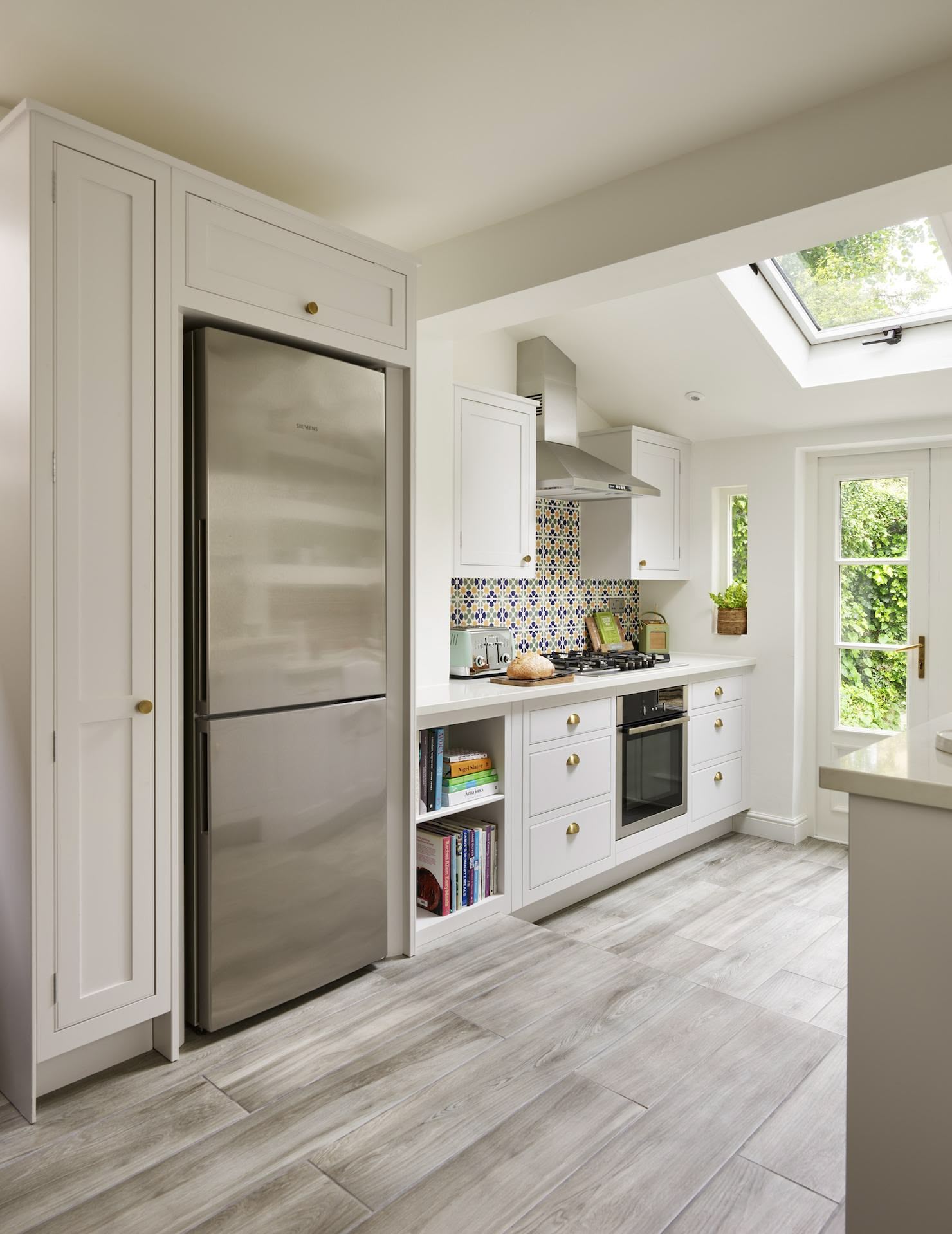 White galley style kitchen featuring a large silver refrigerator surrounded by white Arbor cabinetry