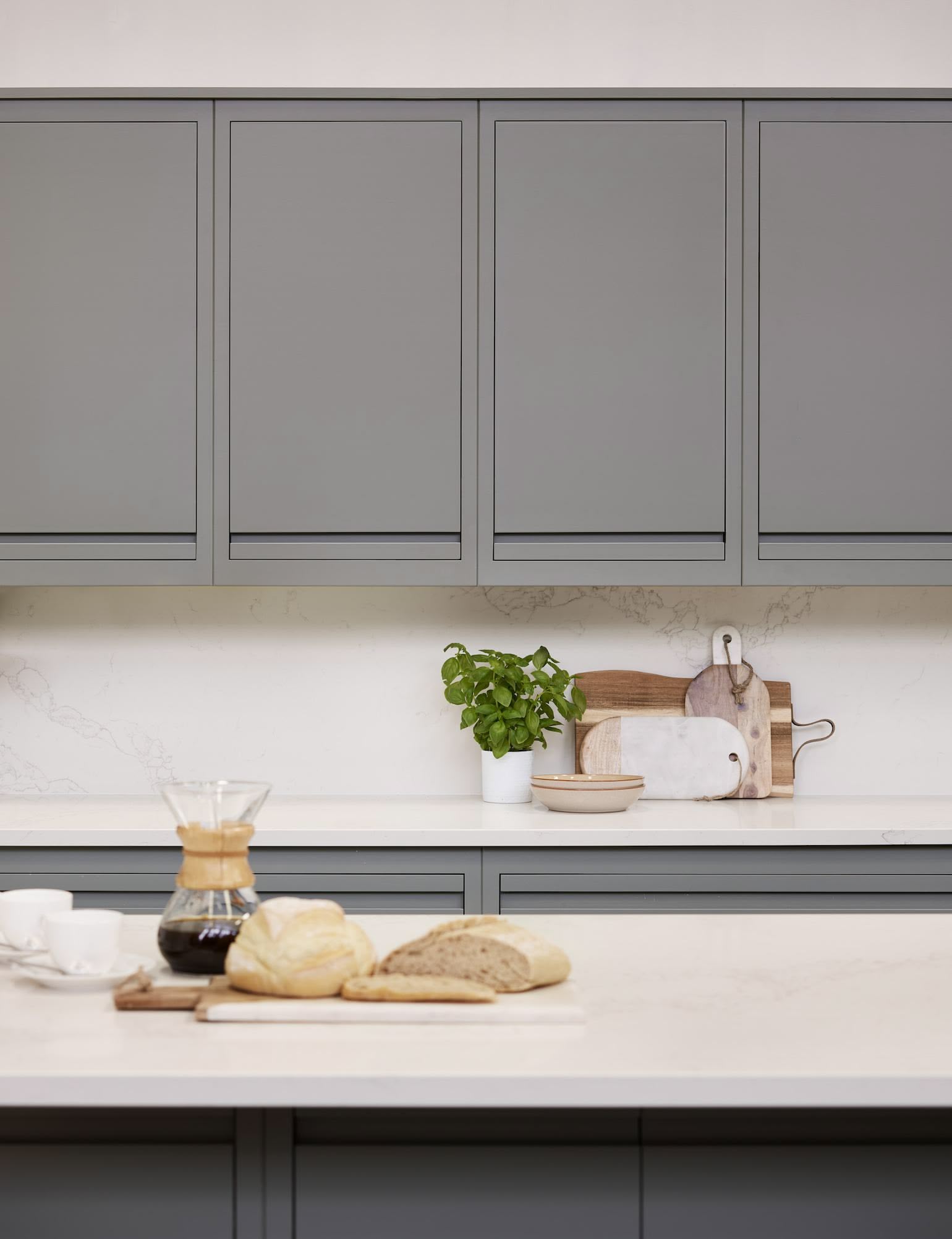 Green-grey Linear Edge kitchen cabinetry and island with white worktops