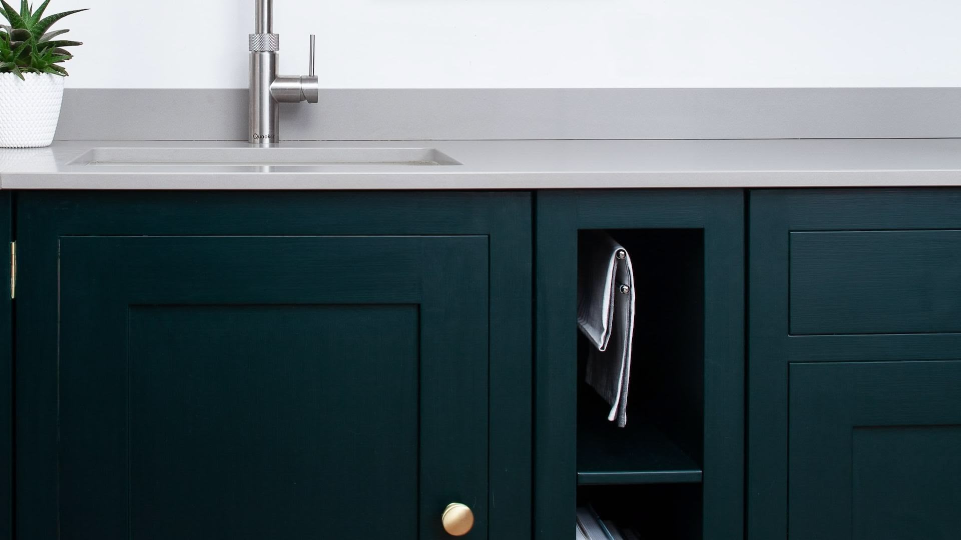 Rich green Shaker kitchen cabinetry with grey worktop and silver tap