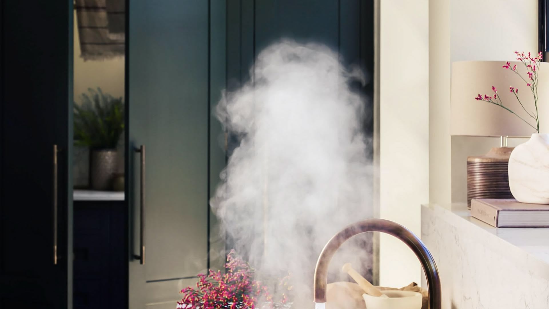 Steaming brass tap in front of dark green Shaker kitchen door open to show hidden utility room