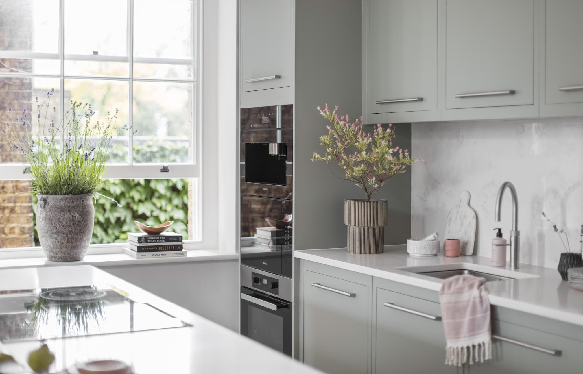 Green-grey Linear kitchen cabinetry with white worktops and silver handles