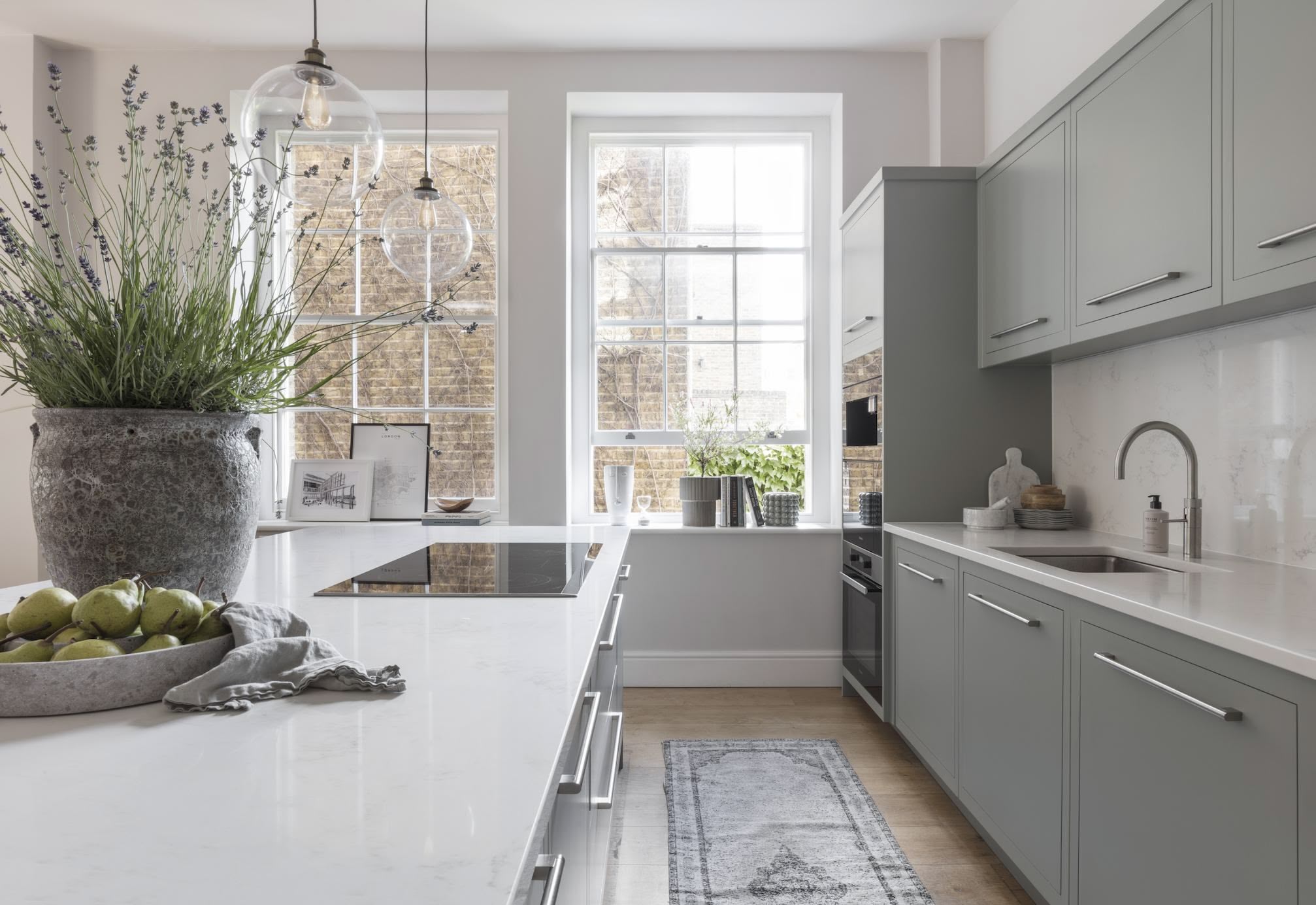 Green-grey Linear kitchen cabinetry with white worktops and silver handles