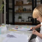 Young child drawing sat at a kitchen island with white worktop