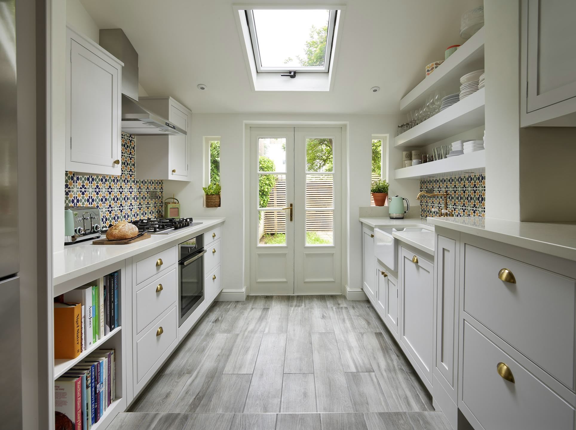 White Shaker kitchen cabinetry with cream worktops and decorative tiled cooker splashback