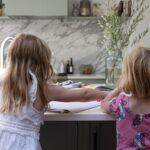 Two children sat at a grey kitchen island with white worktop