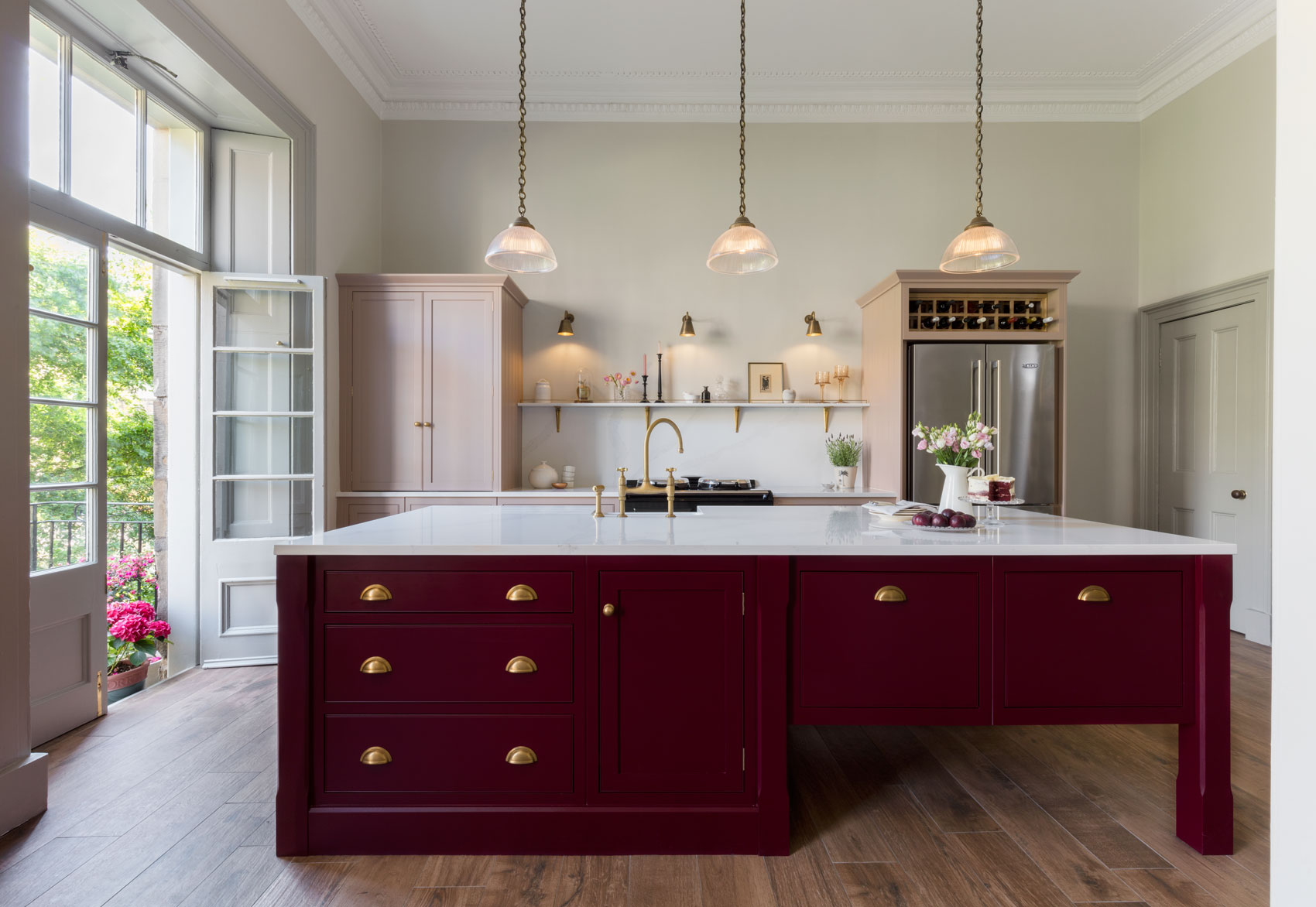 Pink and burgundy kitchen with large island featuring pendant lighting and bespoke design with integrated storage