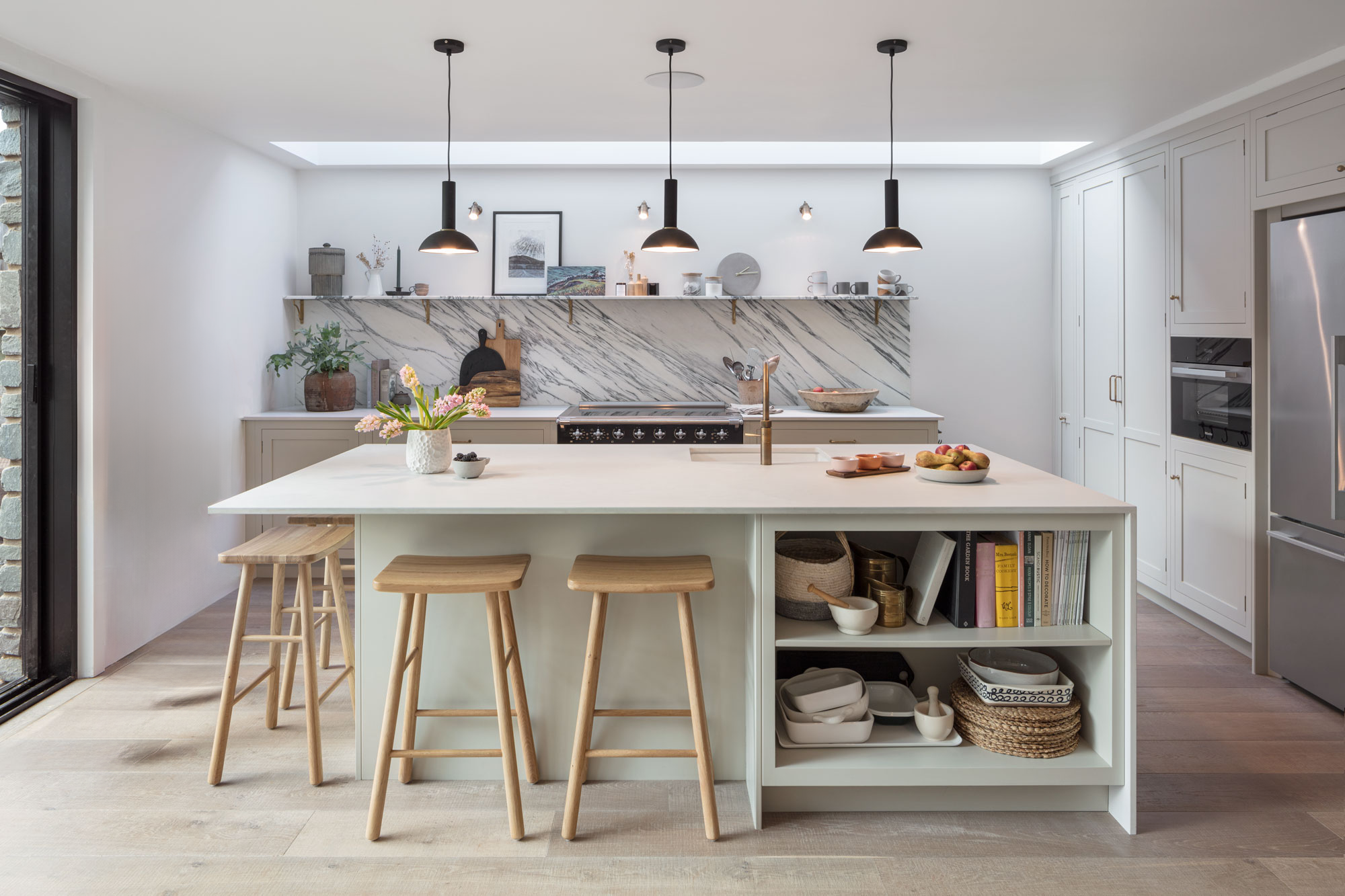 Neutral kitchen design with island with waterfall worktop, integrated seating zone and open storage